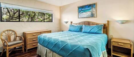 A bedroom with a large bed, a chair, a nightstand, and a window with a view of trees.