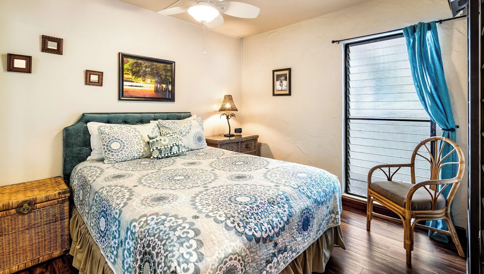 A bedroom with a bed, a nightstand, a lamp, a wicker chest, a chair, and a window with curtains.