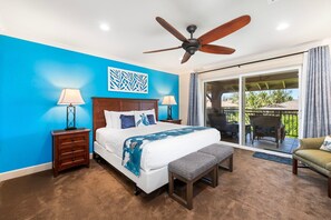 A bedroom with a large bed, a ceiling fan, a nightstand with a lamp, and a view of the outdoors through a sliding glass door.