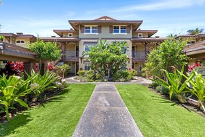 A multi-story hotel with a central courtyard, featuring a well-maintained lawn, potted plants, and a concrete pathway leading to the entrance.