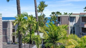 A hotel with a view of the ocean, palm trees, and a parking lot. - Oceanview Kona Condo - Pool, Lanai, Walk to Town - Vrkcv (Kailua-Kona)
