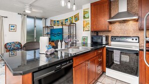 A kitchen with a dishwasher, oven, and microwave. There are wooden cabinets and a tiled backsplash. - Oceanview Kona Condo - Pool, Lanai, Walk to Town - Vrkcv (Kailua-Kona)