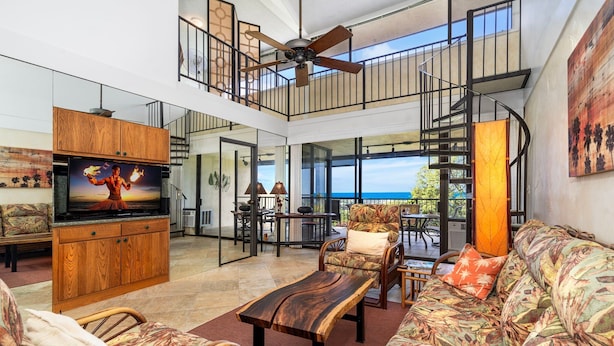 A spacious living area with a large TV, wooden furniture, and a balcony with a view. - 2 Bedrooms + Loft - Sleeps 6 - Ocean & Golf Views - Lanai - Vrkcv (Kailua-Kona)