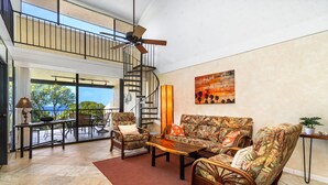 A spacious living area with a high ceiling, a spiral staircase, and a large window offering a view of the outdoors. - 2 Bedrooms + Loft - Sleeps 6 - Ocean & Golf Views - Lanai - Vrkcv (Kailua-Kona)