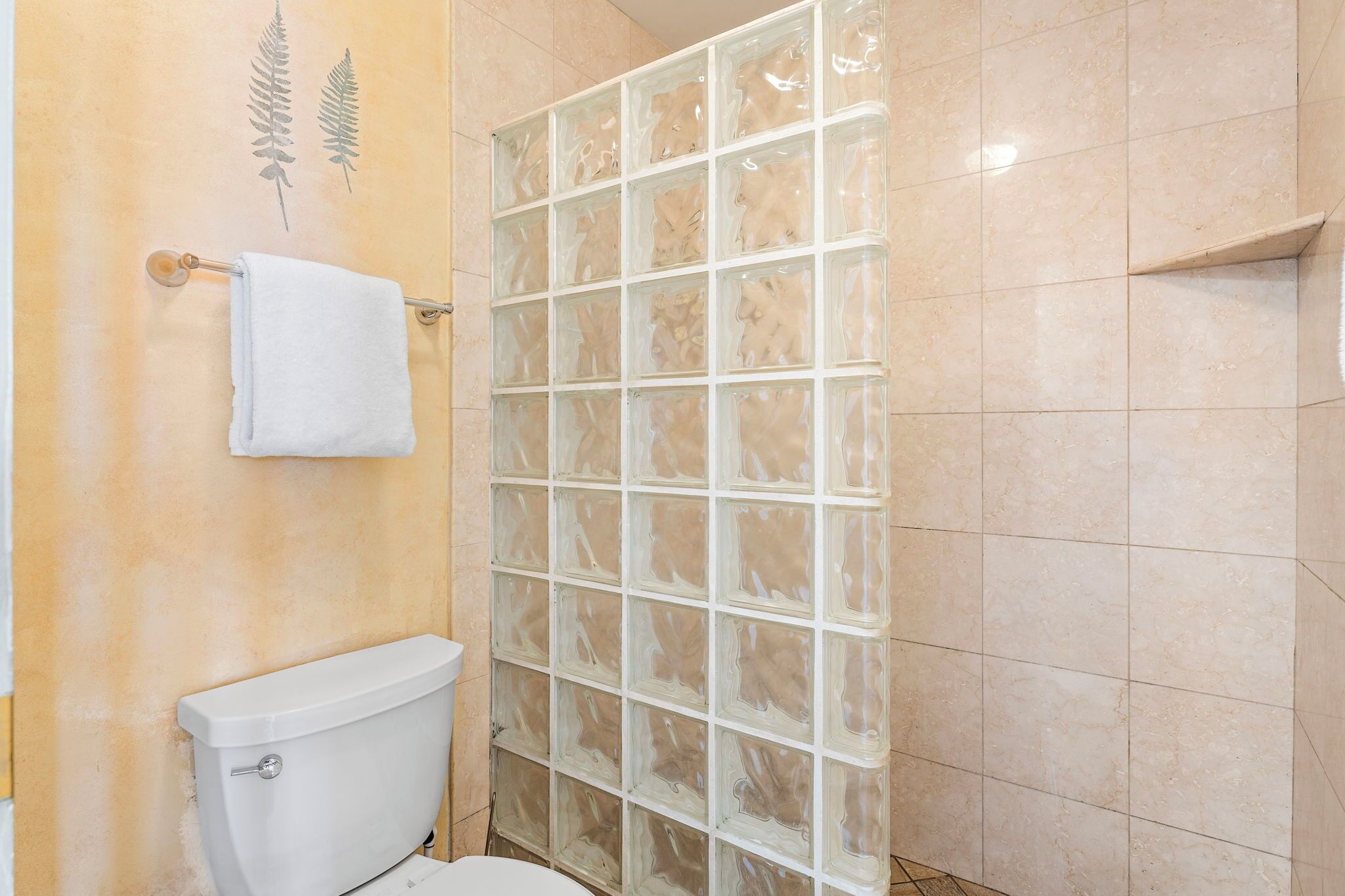 A bathroom with a glass shower enclosure, a white toilet, and a towel rack.