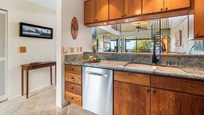 A kitchen with wooden cabinets, a granite countertop, and a dishwasher. - 2 Bedrooms + Loft - Sleeps 6 - Ocean & Golf Views - Lanai - Vrkcv (Kailua-Kona)