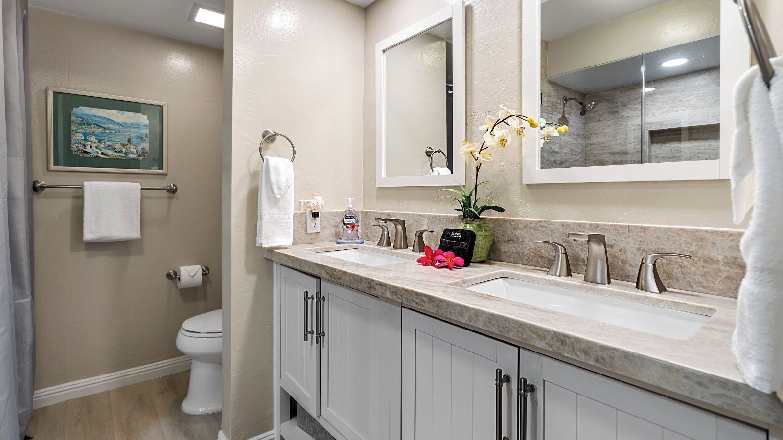 A bathroom with two sinks, a toilet, a towel rack, a framed picture on the wall, and a potted orchid.