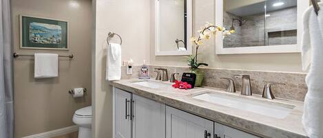 A bathroom with two sinks, a toilet, a towel rack, a framed picture on the wall, and a potted orchid.