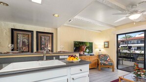 Una cocina con una isla grande, un comedor con mobiliario de mimbre y un balcón con vista a edificios.