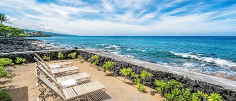 Ett område vid stranden med solstolar och en stenmur.
