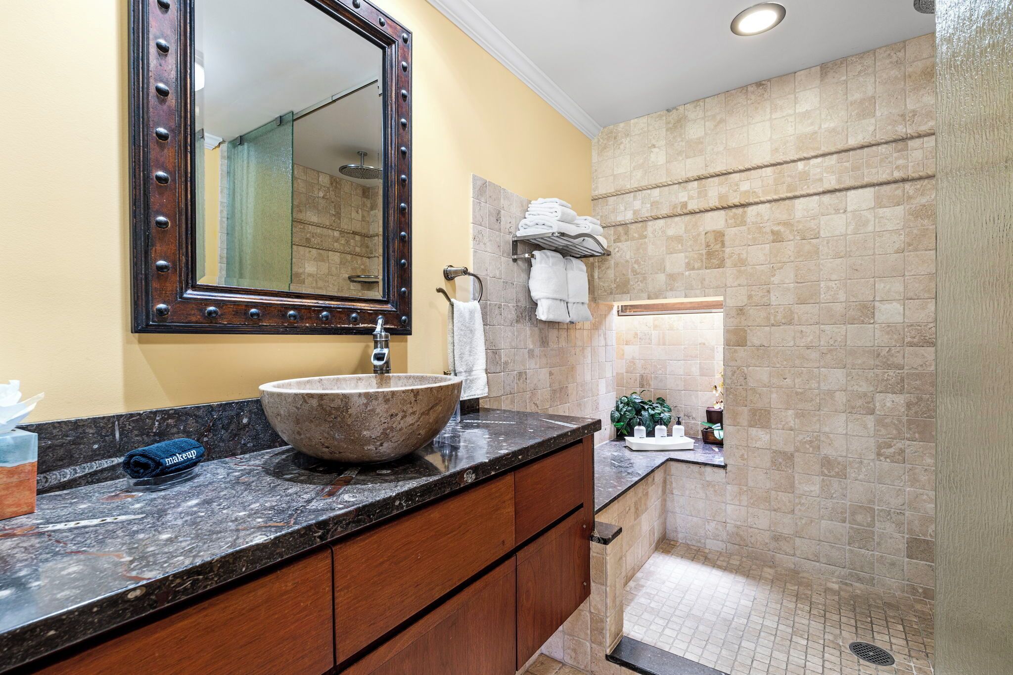 A bathroom with a large vessel sink, a mirror with a decorative frame, a towel rack, and a tiled shower area.