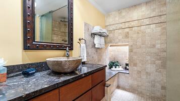 A bathroom with a large vessel sink, a mirror with a decorative frame, a towel rack, and a tiled shower area.