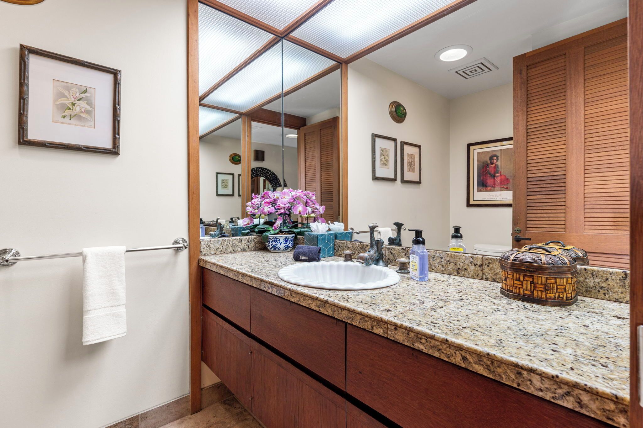 A bathroom with a granite countertop, a white sink, a mirror, and wooden cabinets.