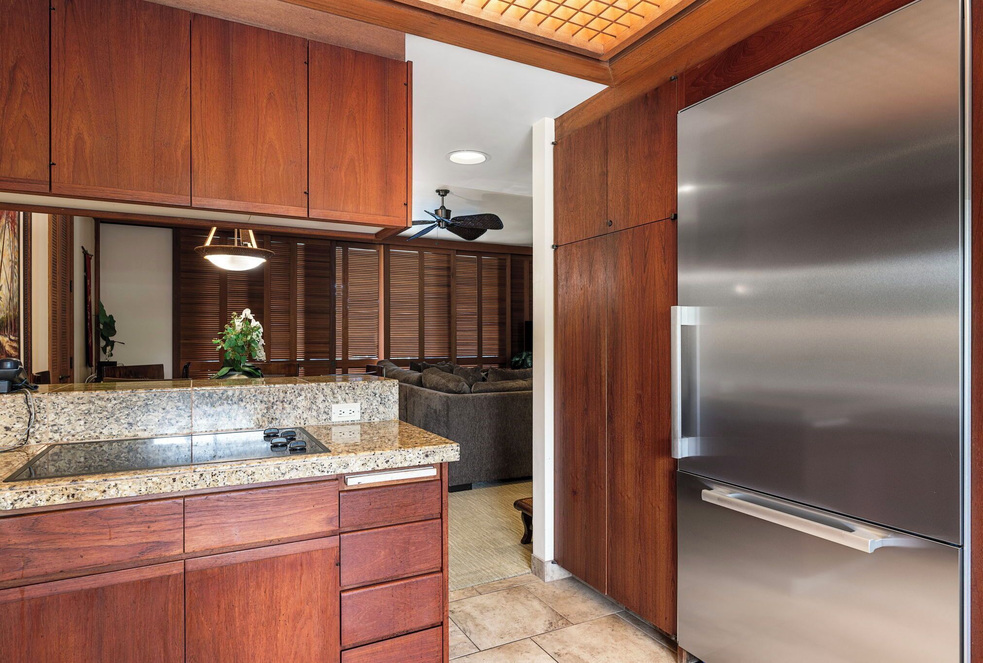 A kitchen with wooden cabinets, a stainless steel refrigerator, granite countertops, and a ceiling fan.