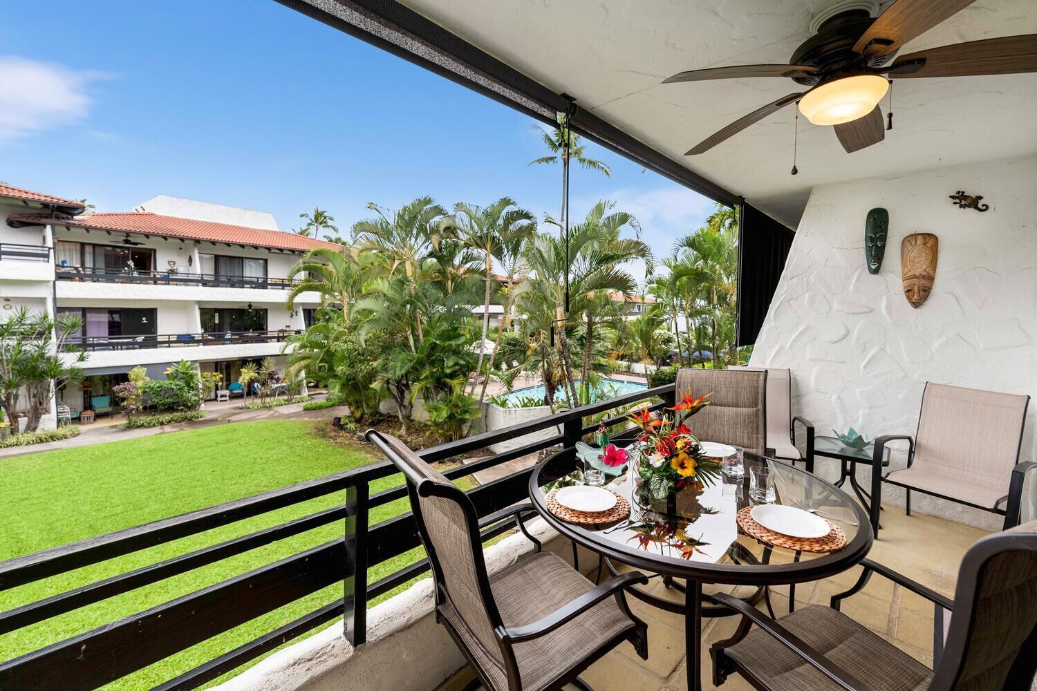 A balcony with a table set for dining, overlooking a pool and palm trees.