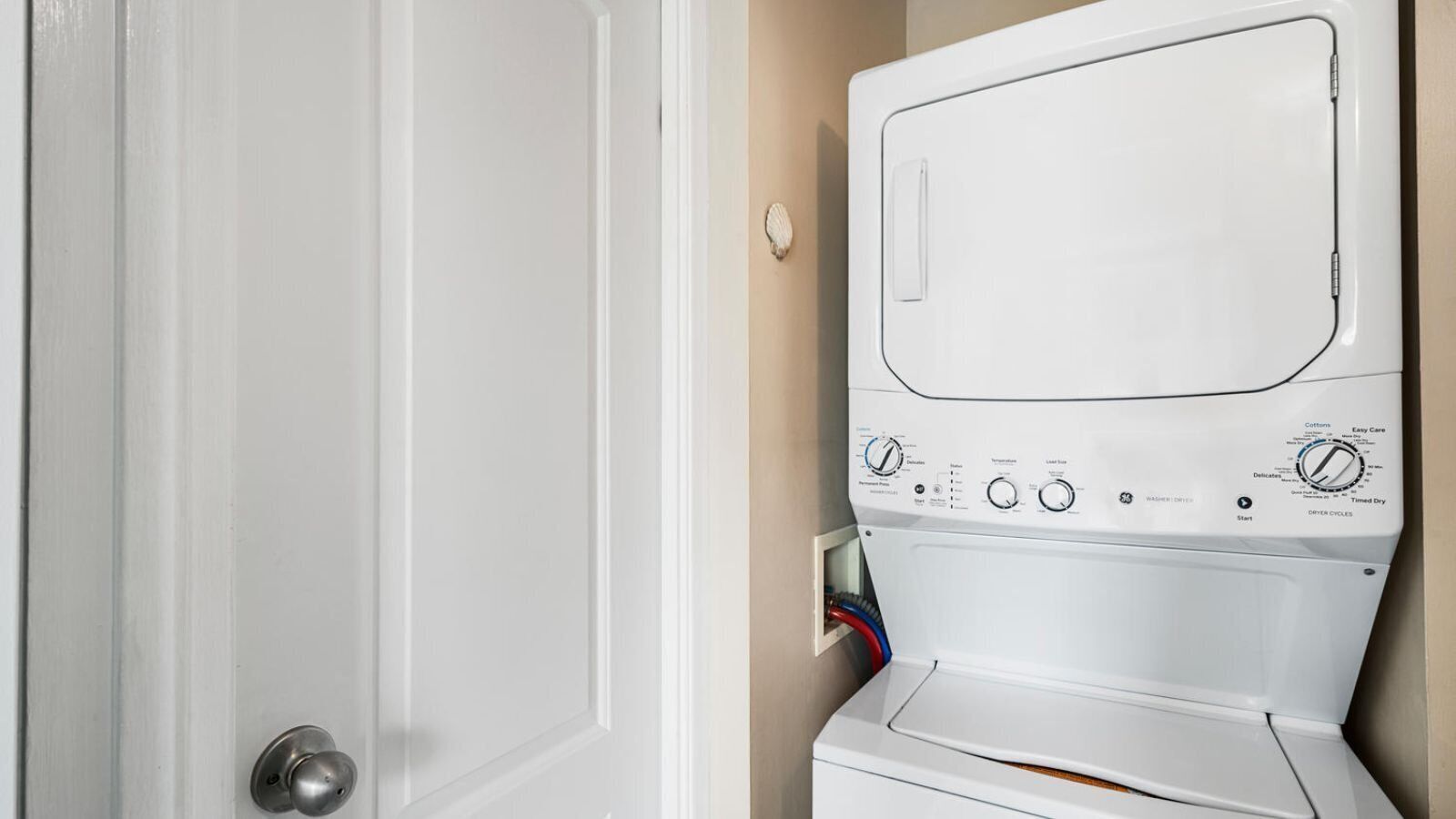 A front-loading washing machine in a laundry room with a door and a wall-mounted control panel.