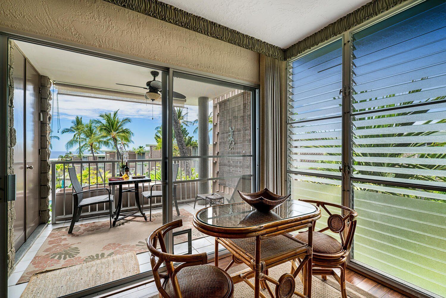 A balcony with a table and chairs, a view of palm trees, and a sliding glass door.