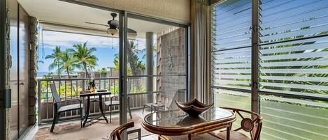 A balcony with a table and chairs, a view of palm trees, and a sliding glass door.