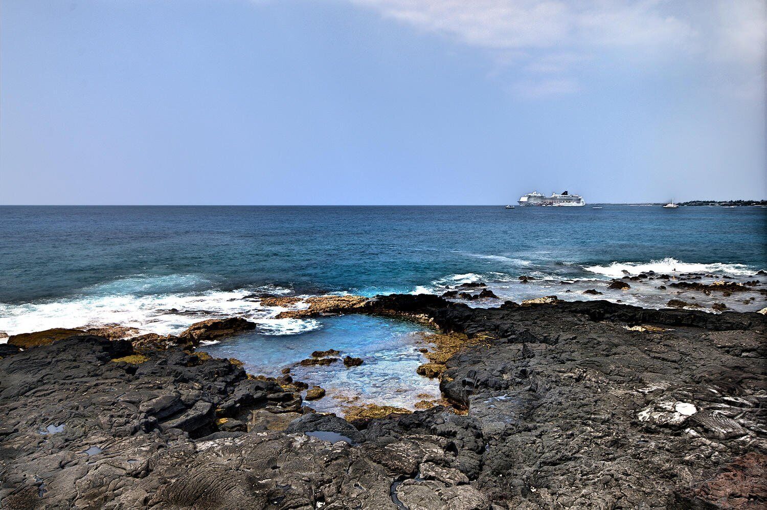 Una costa rocosa con un crucero a lo lejos.