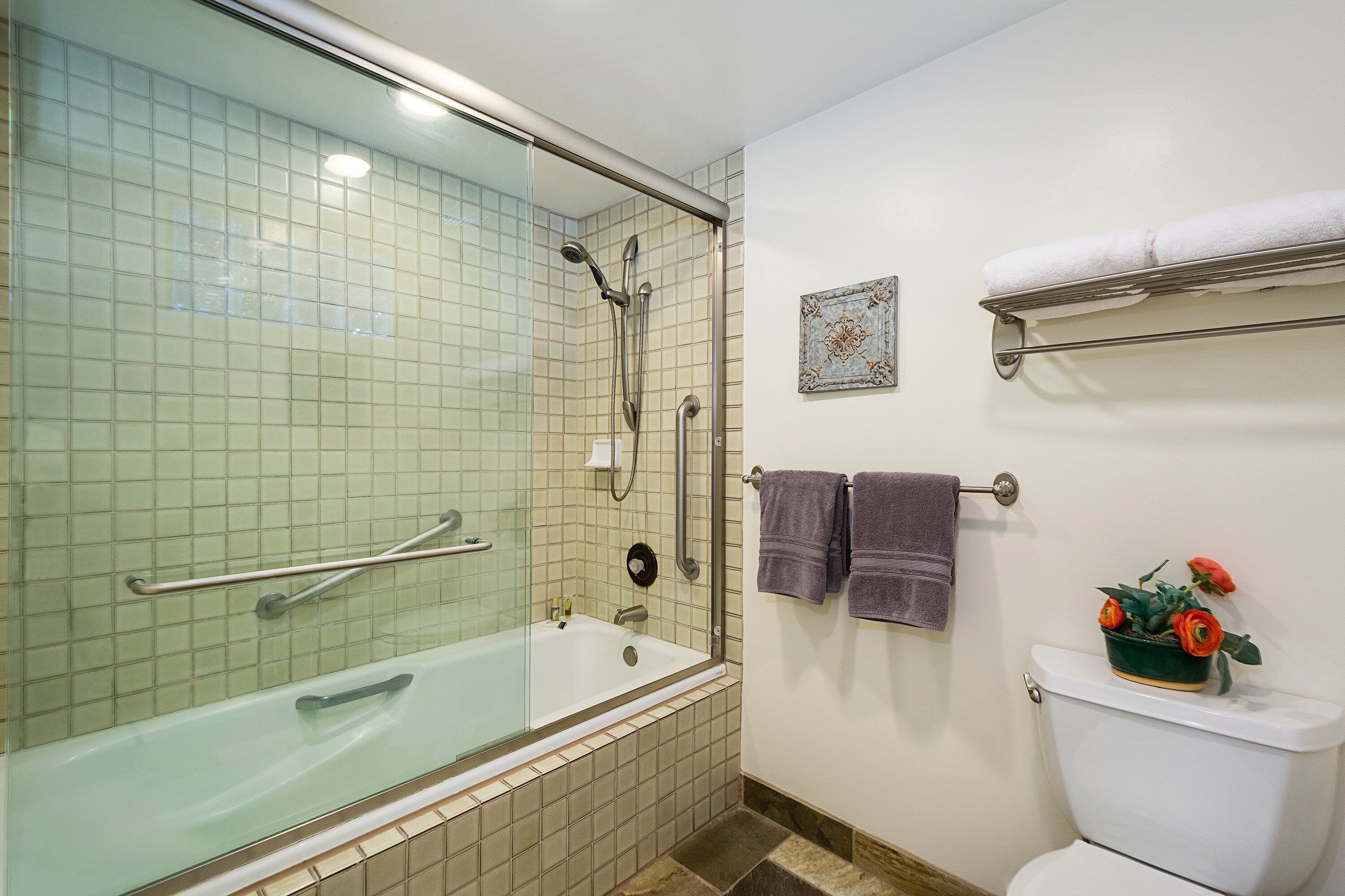 A bathroom with a glass-enclosed shower, a bathtub, a toilet, and a towel rack with towels.