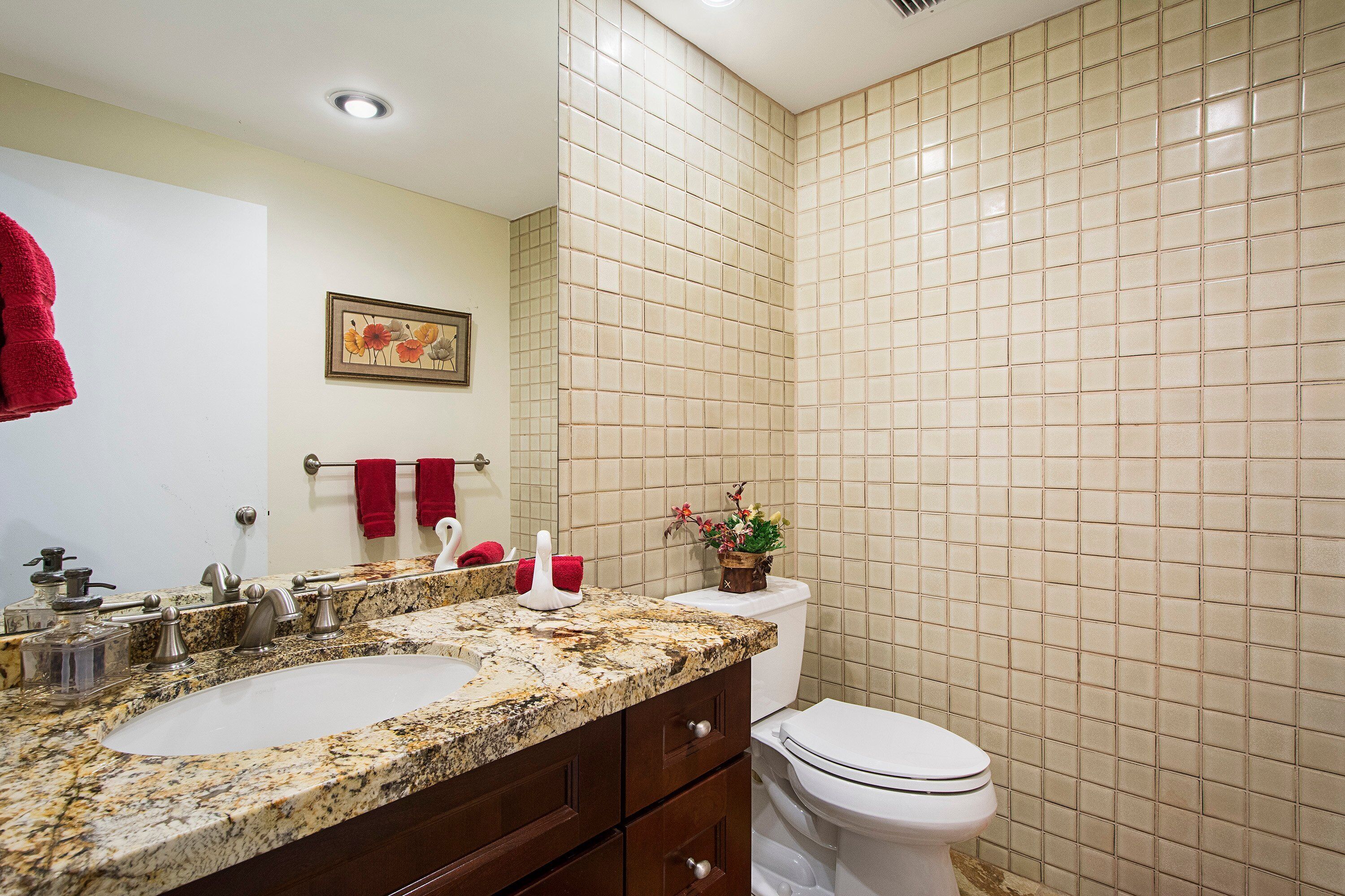 A bathroom with a double sink, a toilet, and a tiled wall.