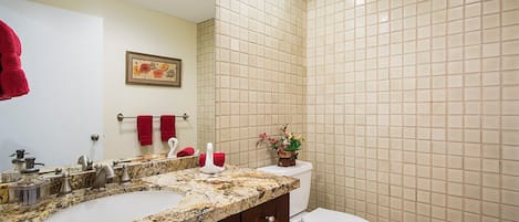 A bathroom with a double sink, a toilet, and a tiled wall.