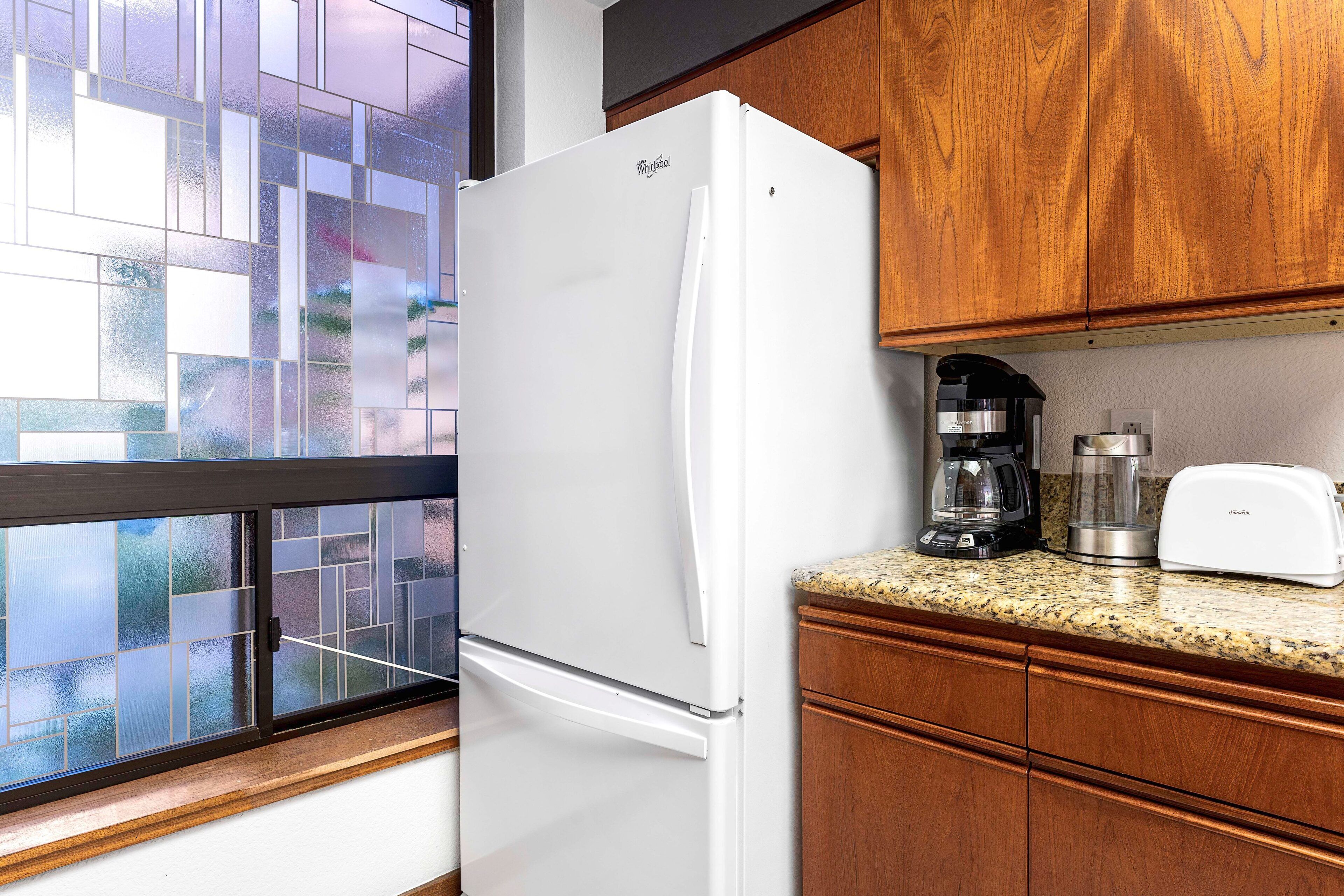 A kitchen with a white refrigerator, wooden cabinets, a granite countertop, a coffee maker, and a toaster.