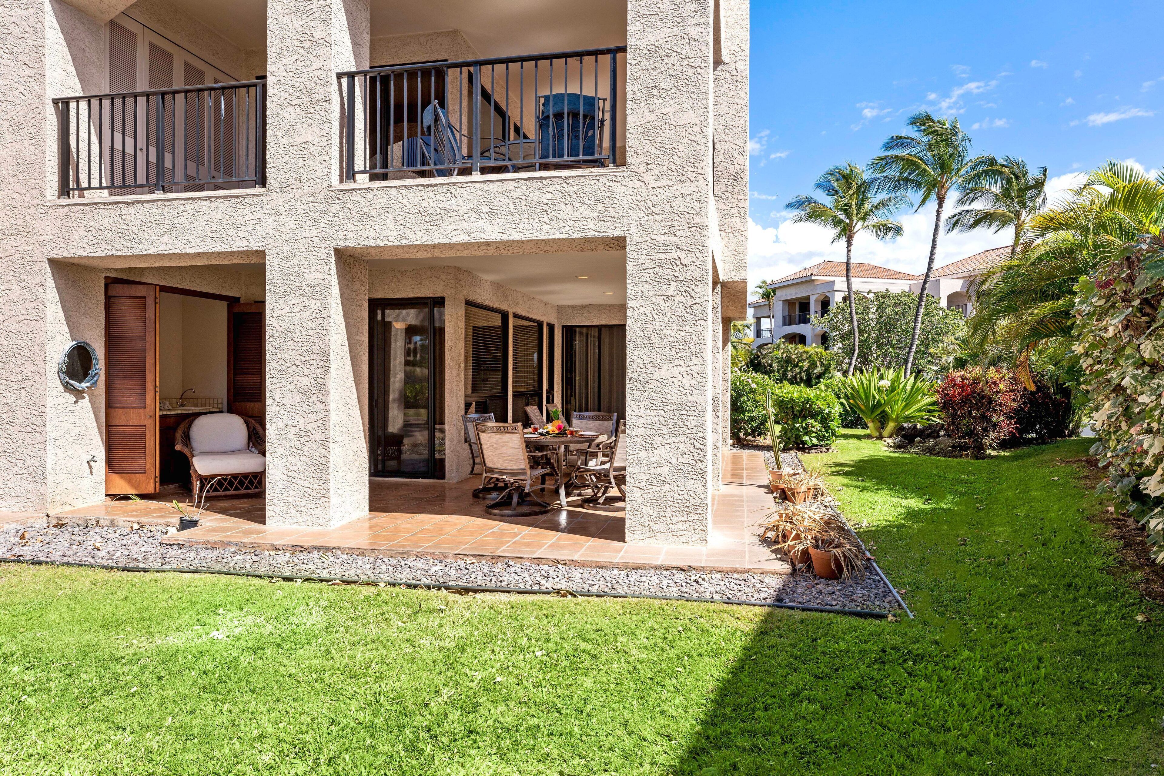 A two-story building with balconies, a patio with outdoor furniture, and a well-maintained garden with palm trees and shrubs.