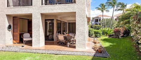 A two-story building with balconies, a patio with outdoor furniture, and a well-maintained garden with palm trees and shrubs.
