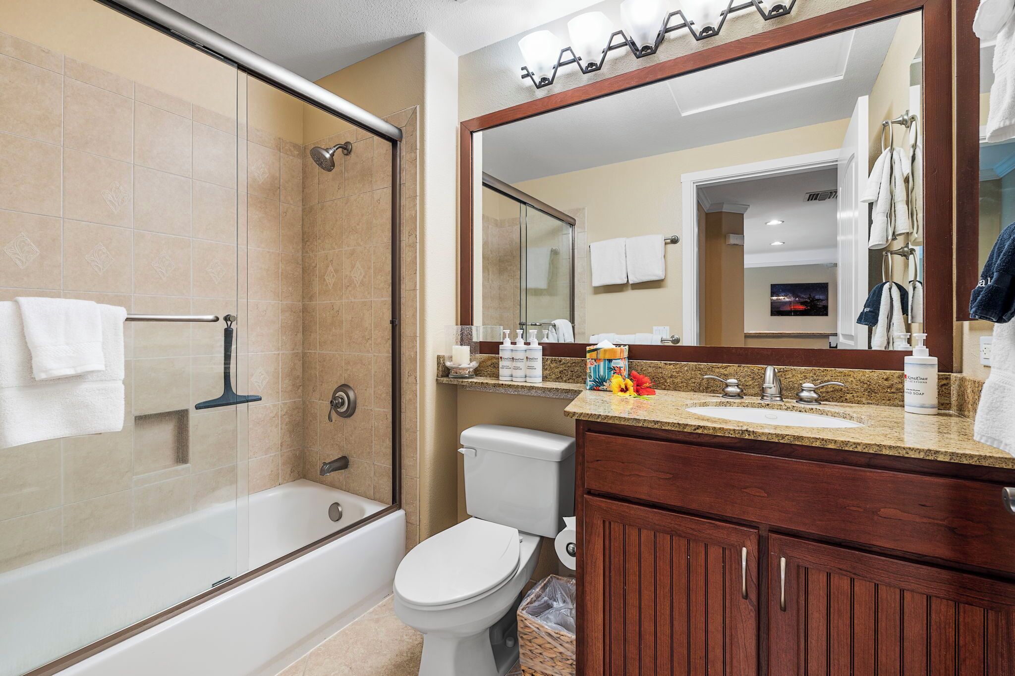 Une salle de bain avec une douche à parois de verre, des toilettes, un lavabo avec un miroir et un meuble-lavabo avec des placards.