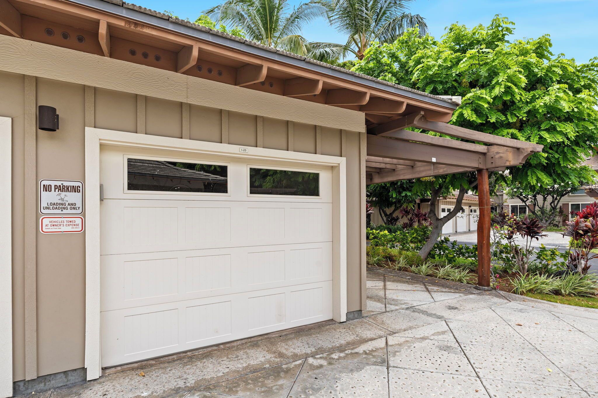 A garage with a 'NO PARKING' sign, a garage door, and a covered parking area with plants.