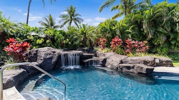 A pool with a waterfall, surrounded by tropical vegetation and palm trees.