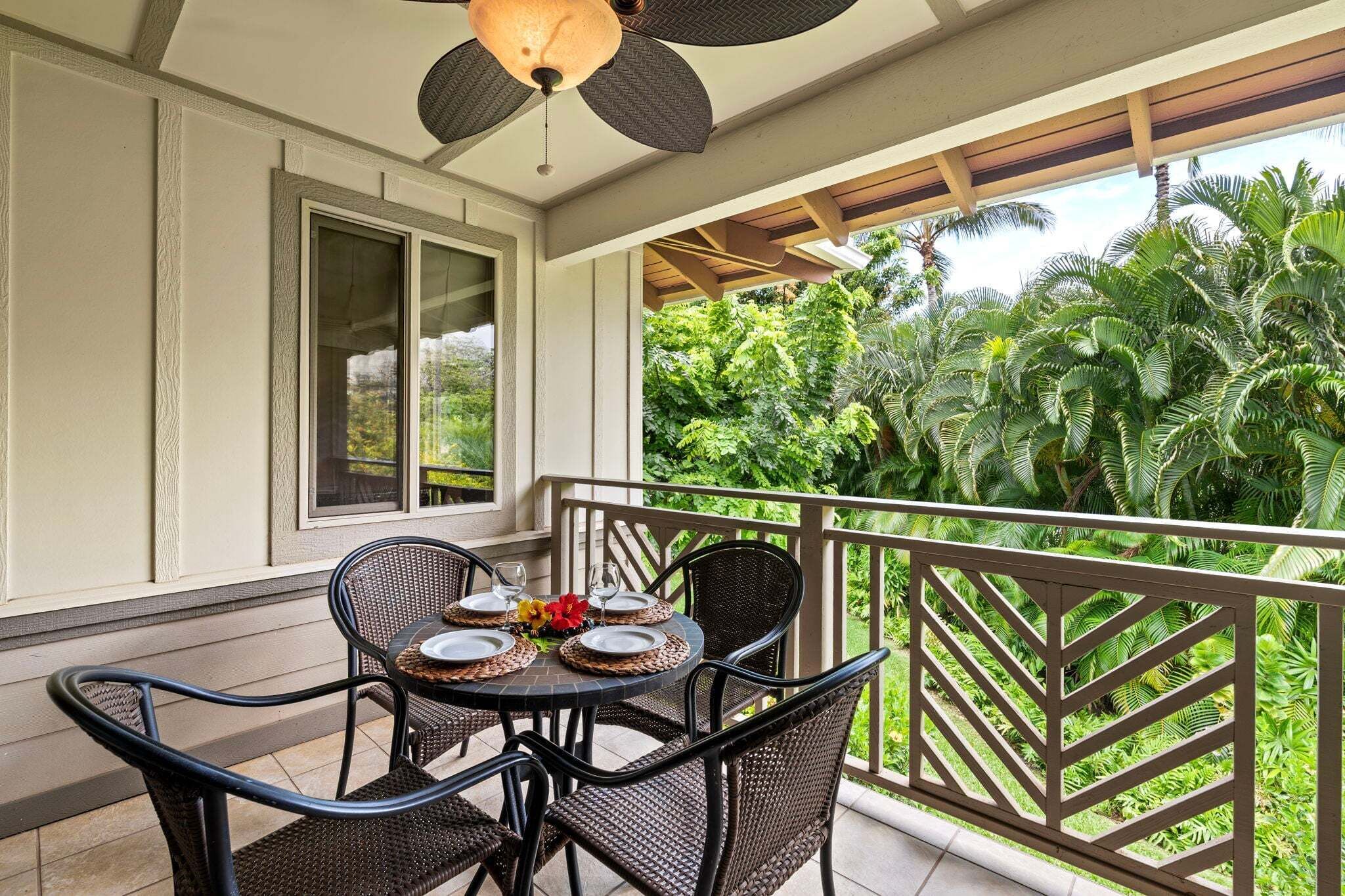 Un balcon avec une table dressée pour deux personnes, entouré de fauteuils en osier, donnant sur une végétation luxuriante.