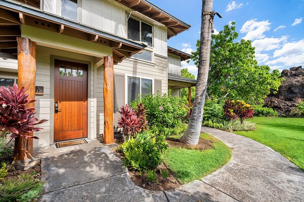 A two-story house with a wooden front door, a number plaque, and a well-maintained lawn. - Easy Walk to the Beach - Golf Community - Concierge Included - Vrkcv (Kamuela)