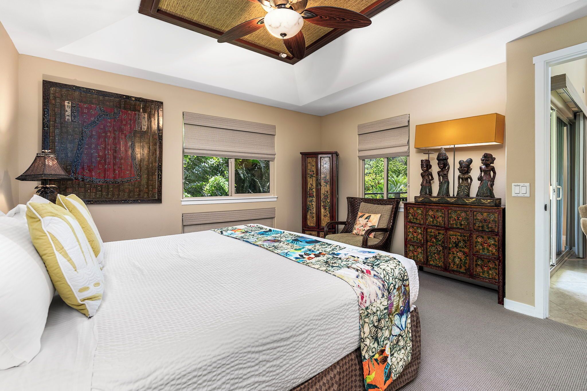 A bedroom with a bed, a ceiling fan, a large window, a dresser, and a lamp.