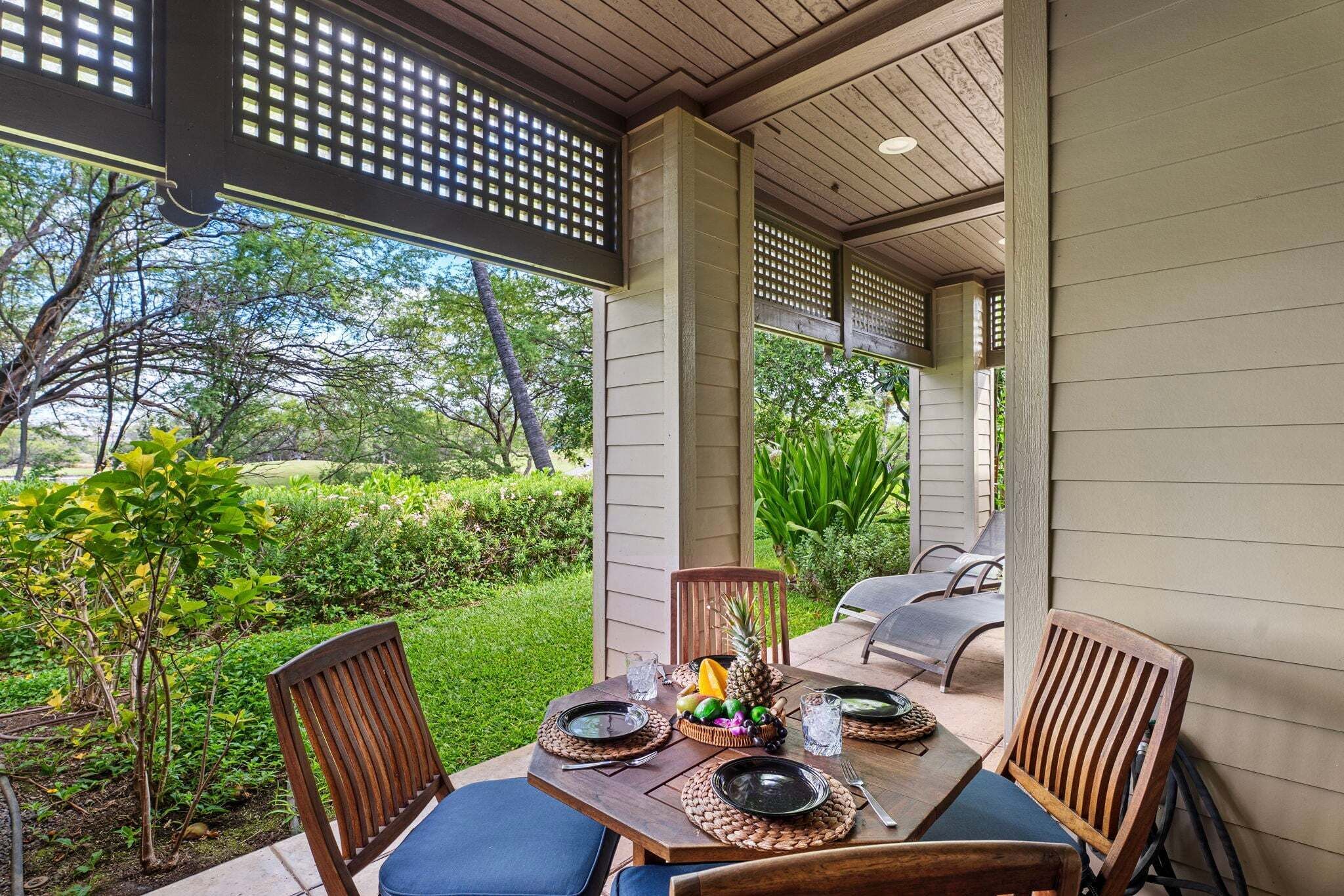 Un patio exterior con una mesa lista para dos personas, rodeado de sillas y vista a un jardín exuberante.