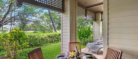 Un patio exterior con una mesa lista para dos personas, rodeado de sillas y vista a un jardín exuberante.