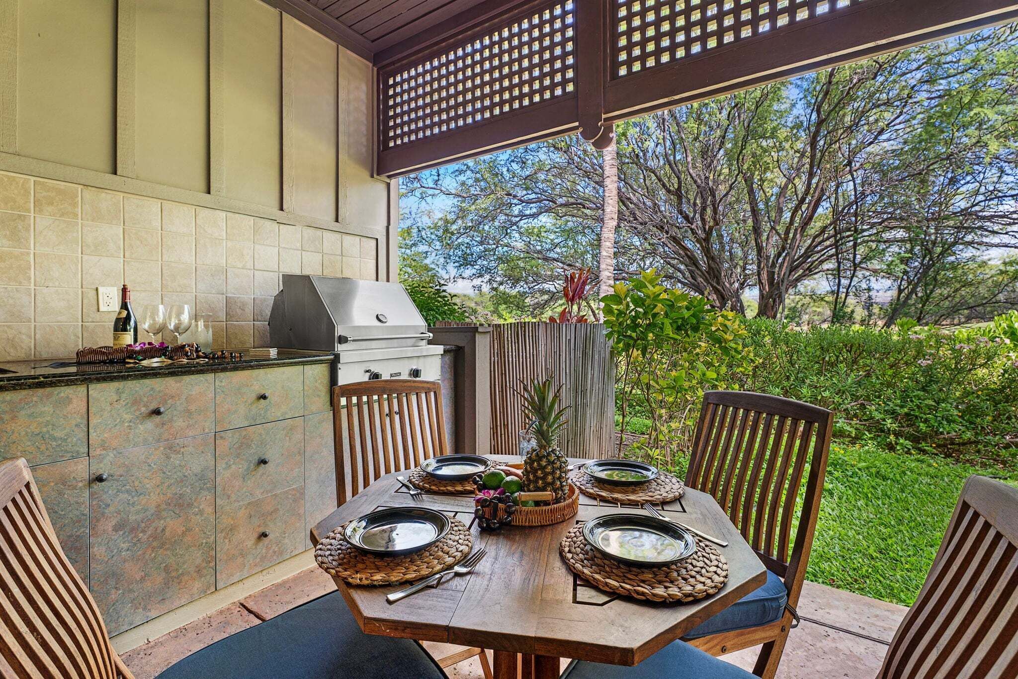 Un espace extérieur aménagé pour les repas, avec un barbecue, une table pour quatre personnes et une vue sur le jardin.