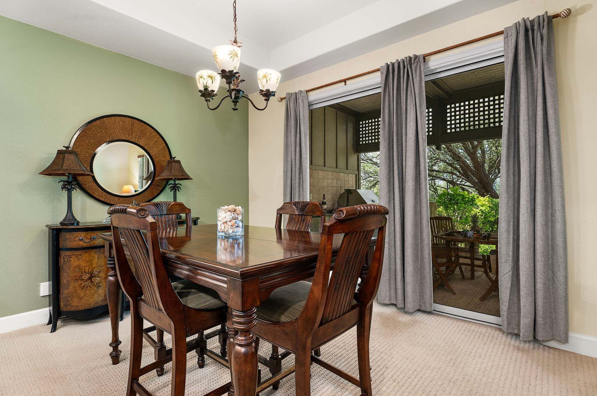 A dining room with a wooden table, chairs, a chandelier, a mirror, and a view through a glass door.