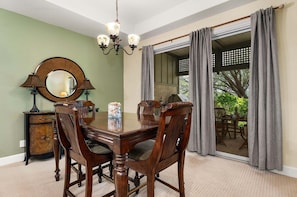 A dining room with a wooden table, chairs, a chandelier, a mirror, and a view through a glass door.