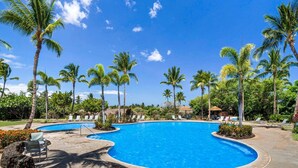 Una piscina con sillones de descanso y palmeras.