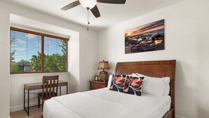 Un dormitorio con cama, escritorio, silla, mesita de noche, lámpara y un cuadro en la pared.