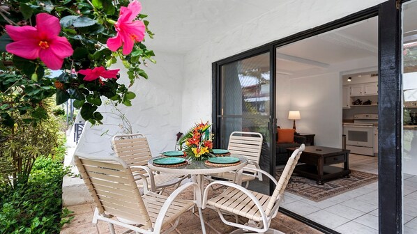 Une terrasse extérieure avec une table ronde et des chaises, un arrangement floral et une vue sur l’intérieur de la maison.