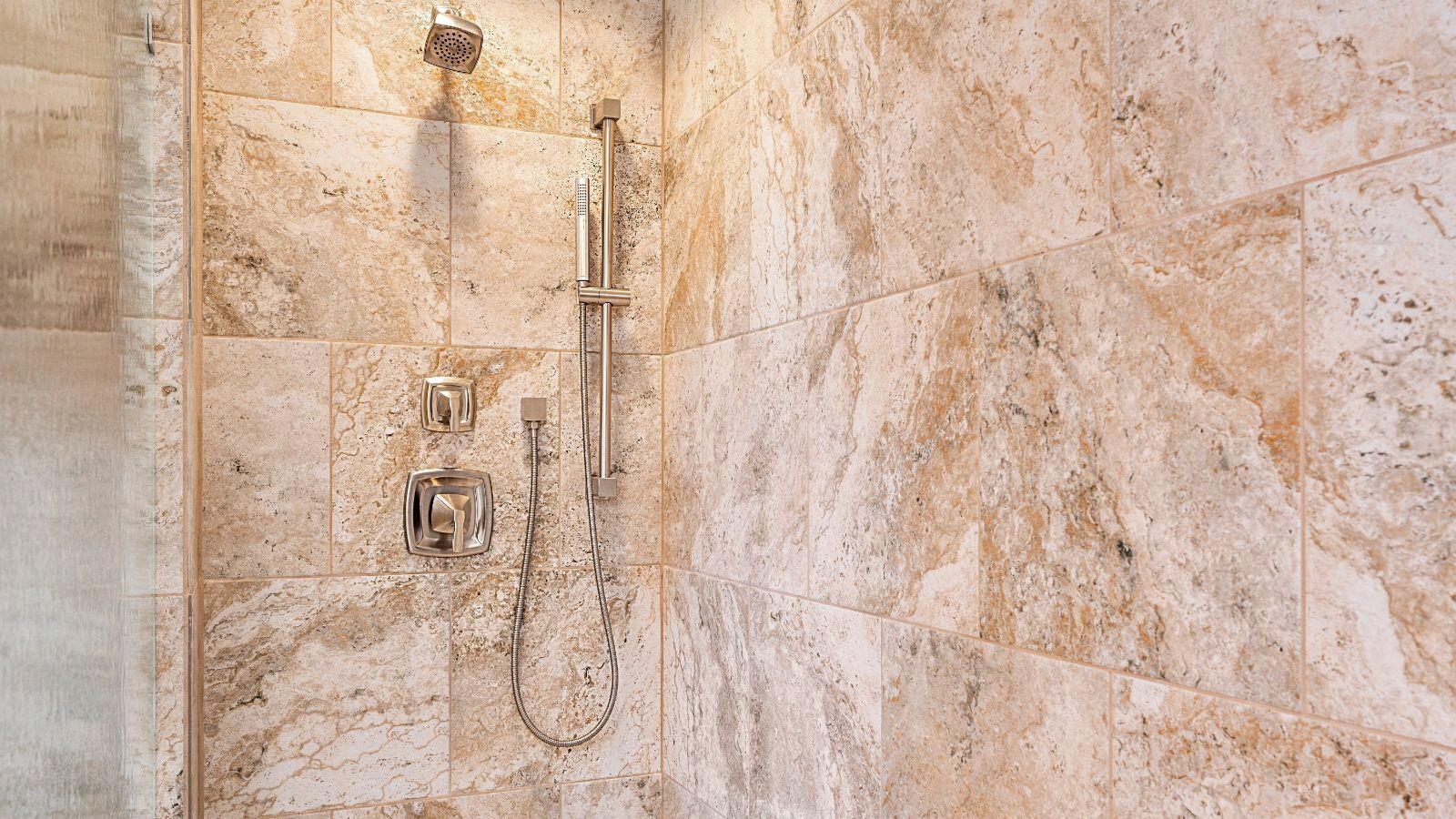 A shower area with a handheld showerhead and a fixed showerhead, both mounted on a tiled wall.