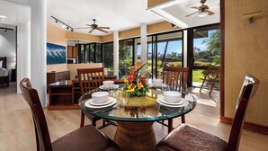 A dining area with a glass table, chairs, and a view of the outdoors. - Luxury Golfside Condo w/ Ocean Views, Central AC & Beach Club - Vrkcv (Kamuela)