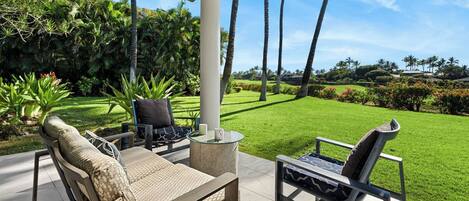 A covered outdoor seating area with two chairs and a table, surrounded by lush greenery and a well-maintained lawn.