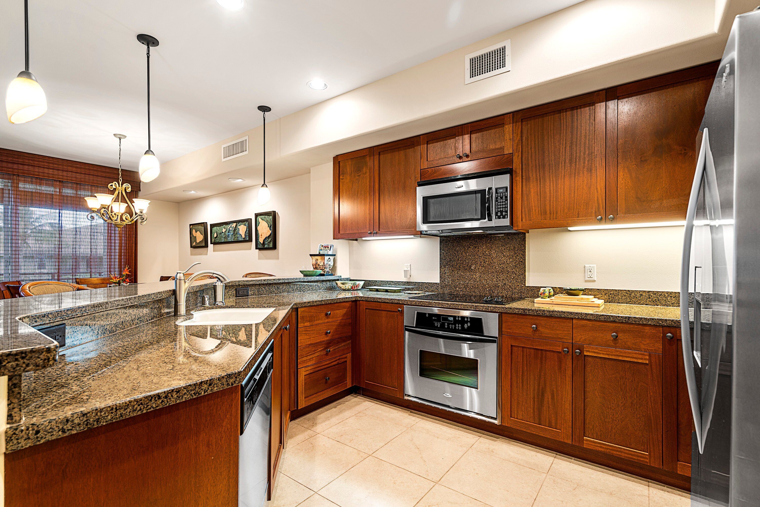 A modern kitchen with granite countertops, stainless steel appliances, wooden cabinets, and pendant lighting.
