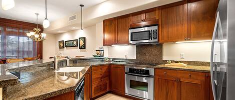 A modern kitchen with granite countertops, stainless steel appliances, wooden cabinets, and pendant lighting.