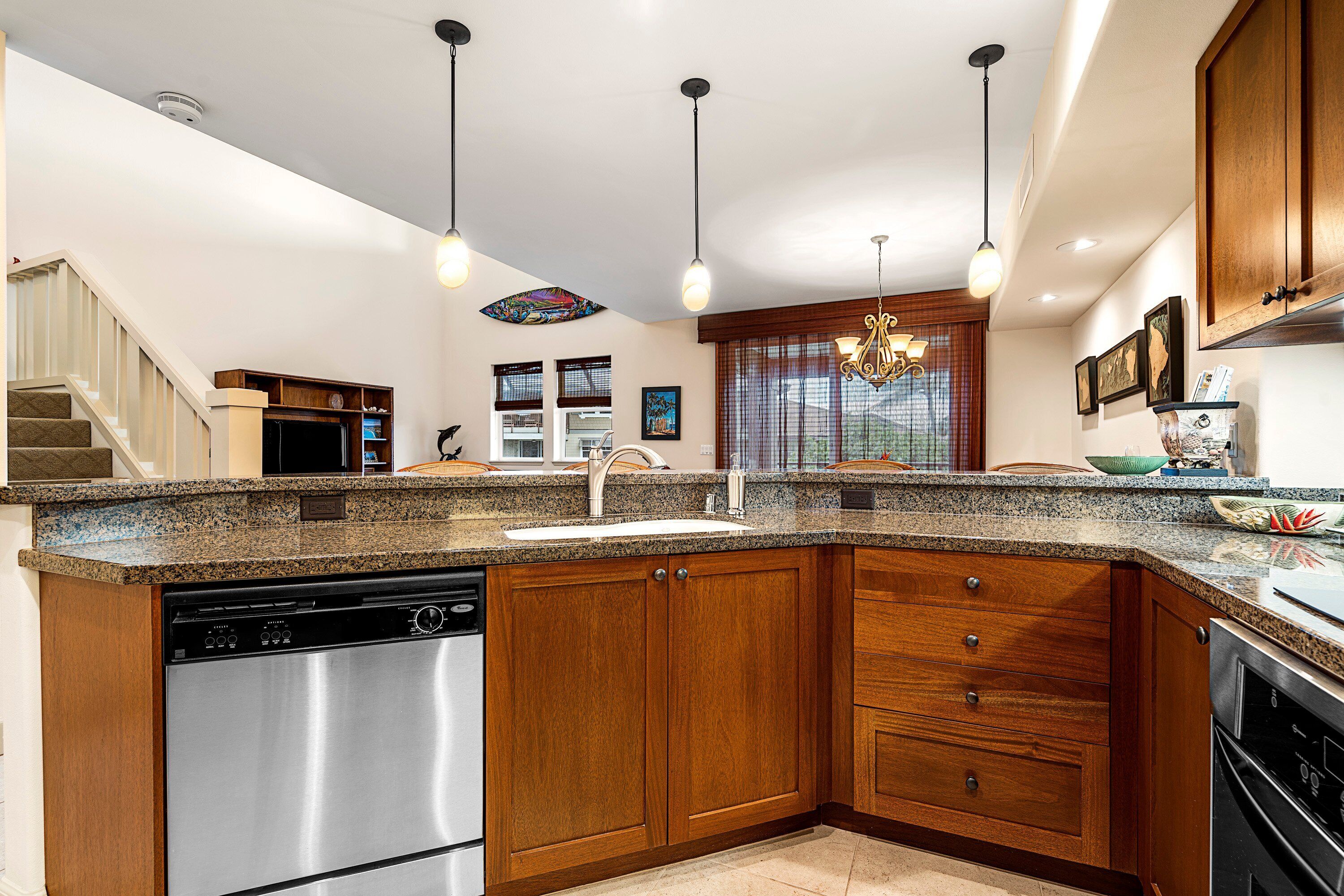 Una cocina con encimeras de granito, gabinetes de madera, electrodomésticos de acero inoxidable e iluminación colgante.