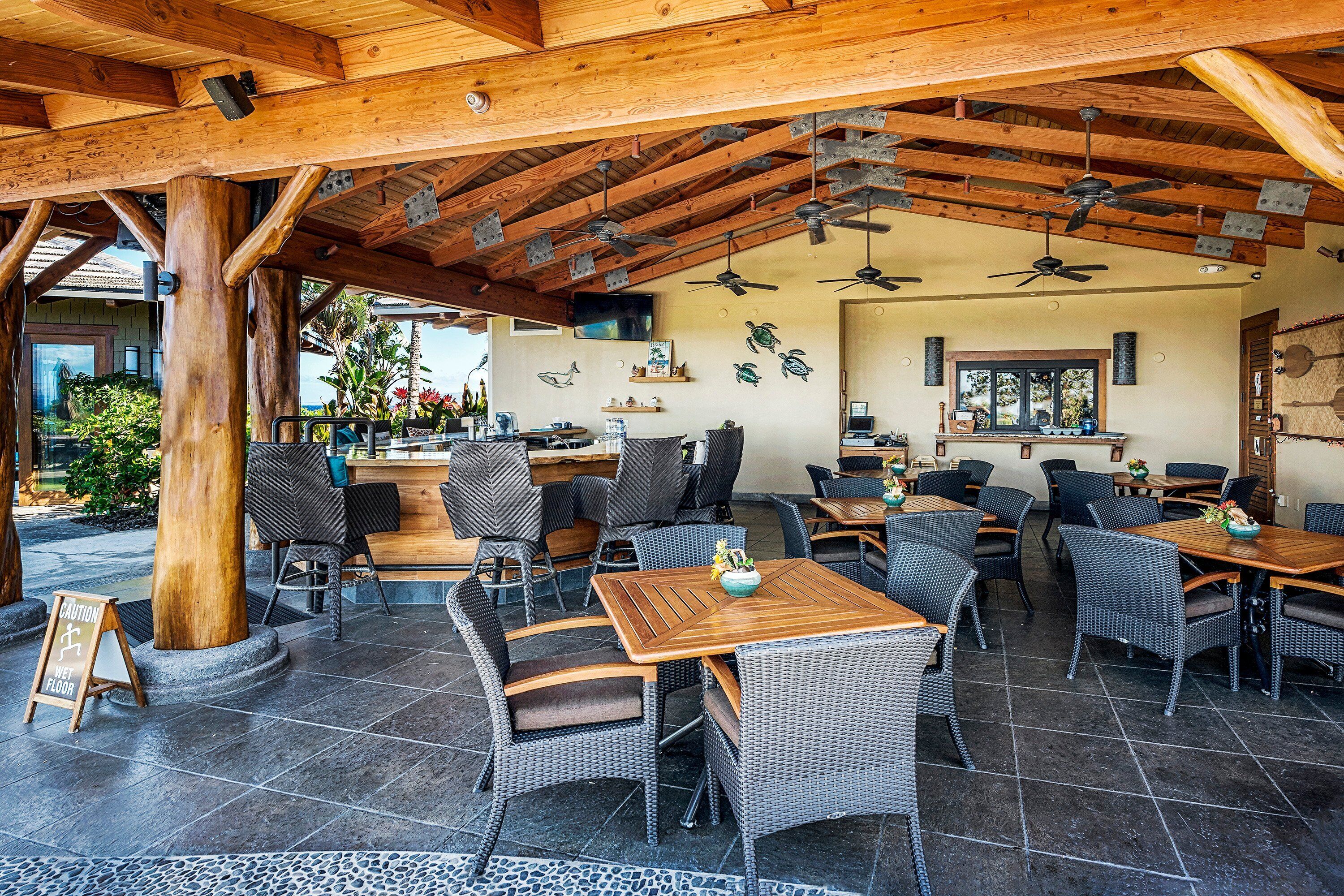 An outdoor patio area with wicker furniture, wooden tables, and ceiling fans.
